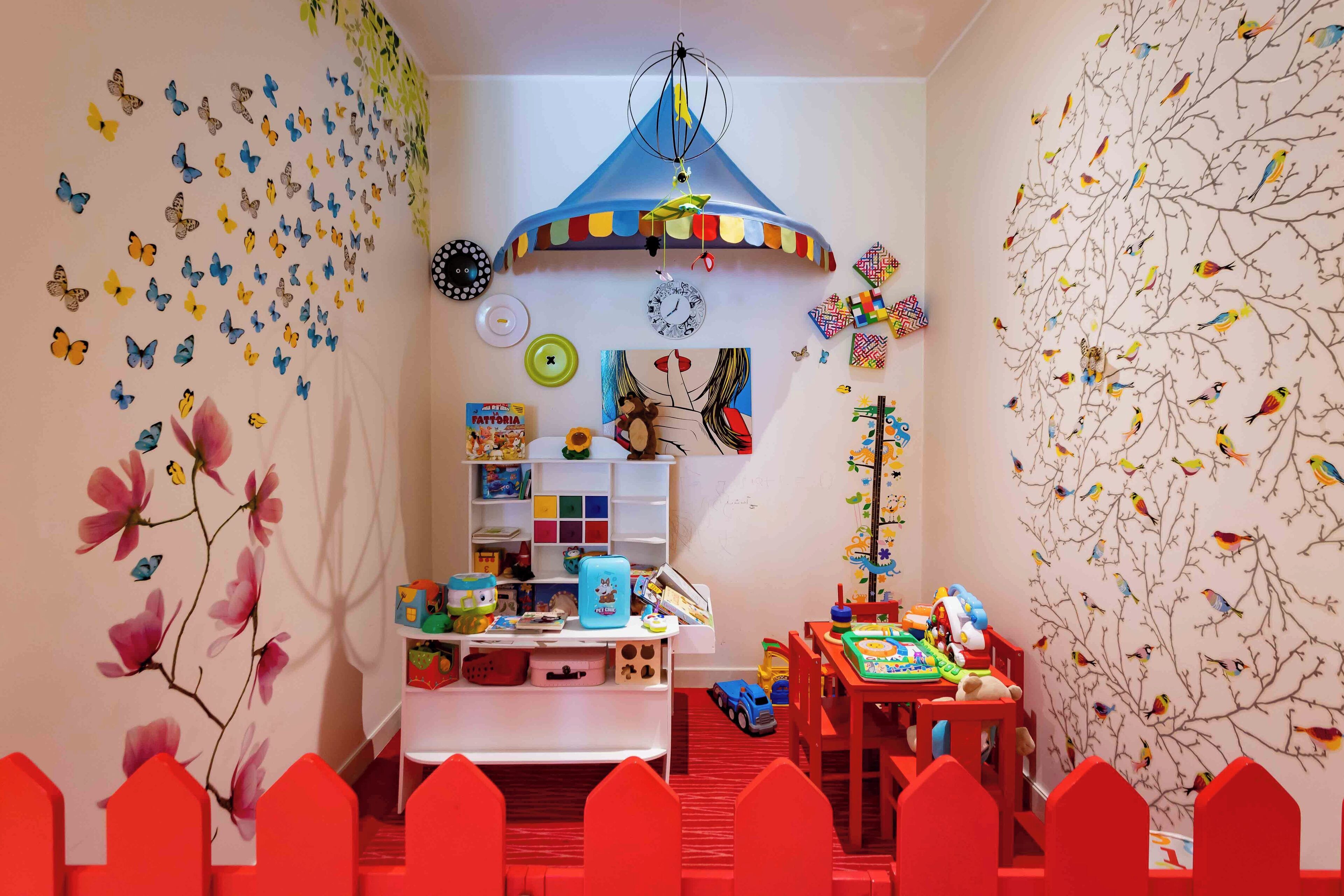 A child's playroom with a colorful butterfly wall decal, a hanging mobile, and a bookshelf filled with toys.