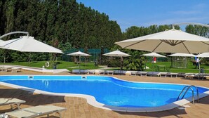 Piscina con sillas de descanso y sombrillas, rodeada de zonas boscosas.