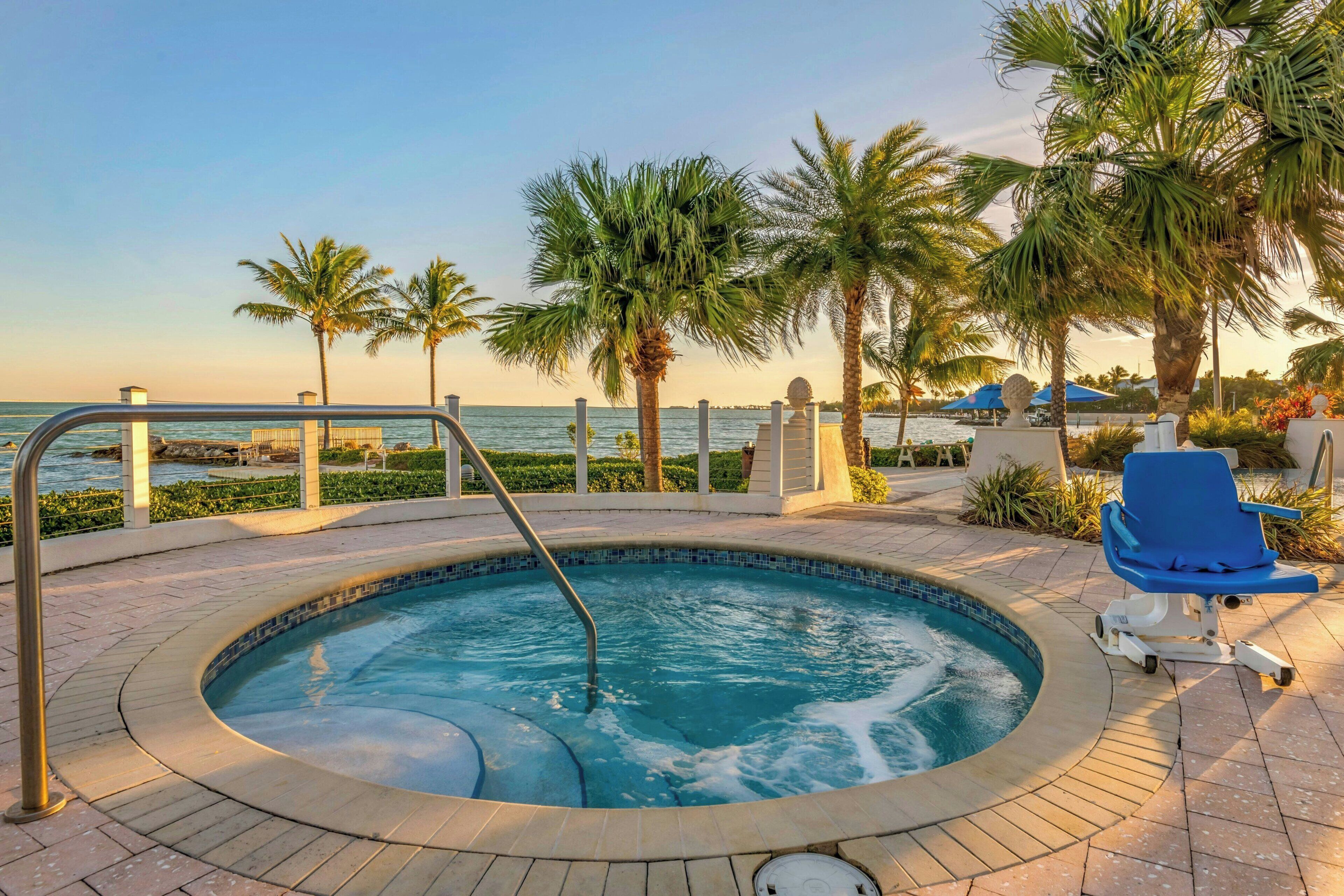 Un jacuzzi avec vue sur la mer, entouré de palmiers et agrémenté d’un fauteuil de relaxation.