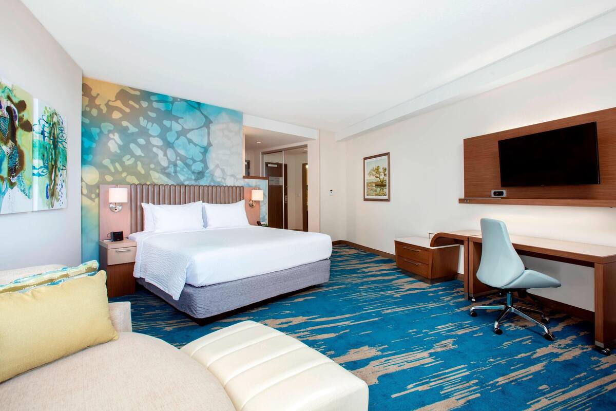 A hotel room with a bed, a desk, a chair, a TV, and artwork on the walls.