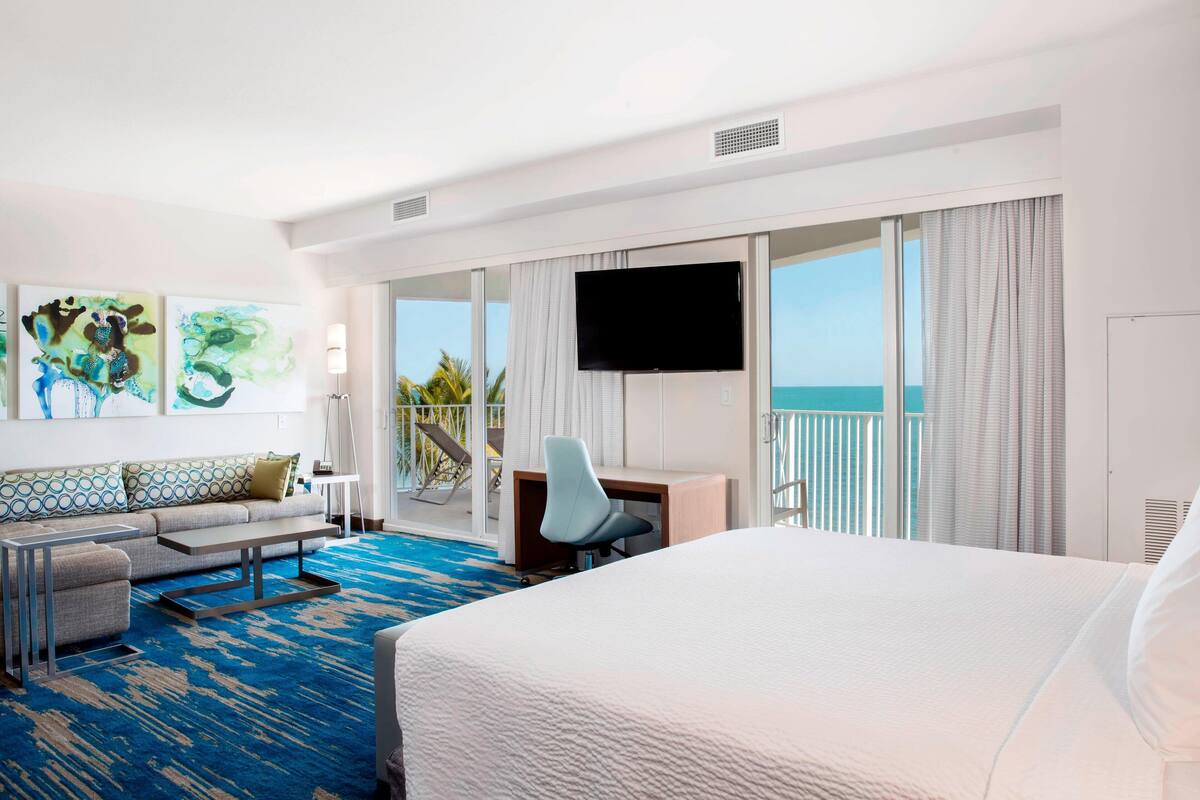 A hotel room with a large bed, a desk, a chair, a sofa, and a TV.