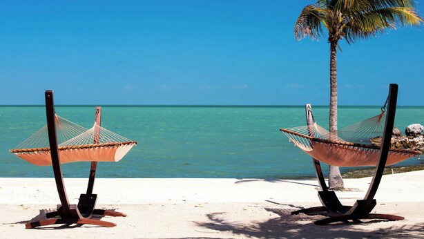 Two hammocks on a sandy beach with a clear blue sky and turquoise water.