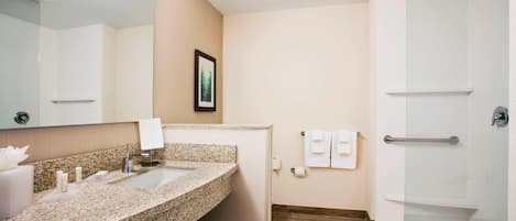 Un baño moderno con lavamanos de granito, un espejo grande, un cuadro en la pared y un box de ducha de vidrio.
