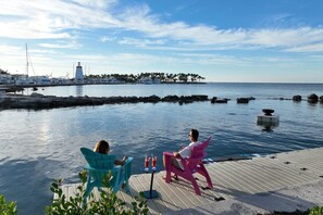 A waterfront scene with a dock, two people sitting on chairs, and a lighthouse in the background. - Courtyard by Marriott Faro Blanco Resort, Marathon Florida Keys (Marathon)