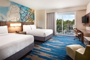 A hotel room with two beds, a desk, a chair, a TV, and a balcony with a view of palm trees.