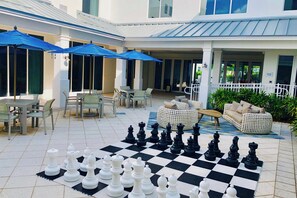 A spacious outdoor area with a large checkered chessboard, outdoor seating, and umbrellas.