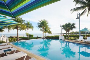 A pool area with lounge chairs, palm trees, and umbrellas.