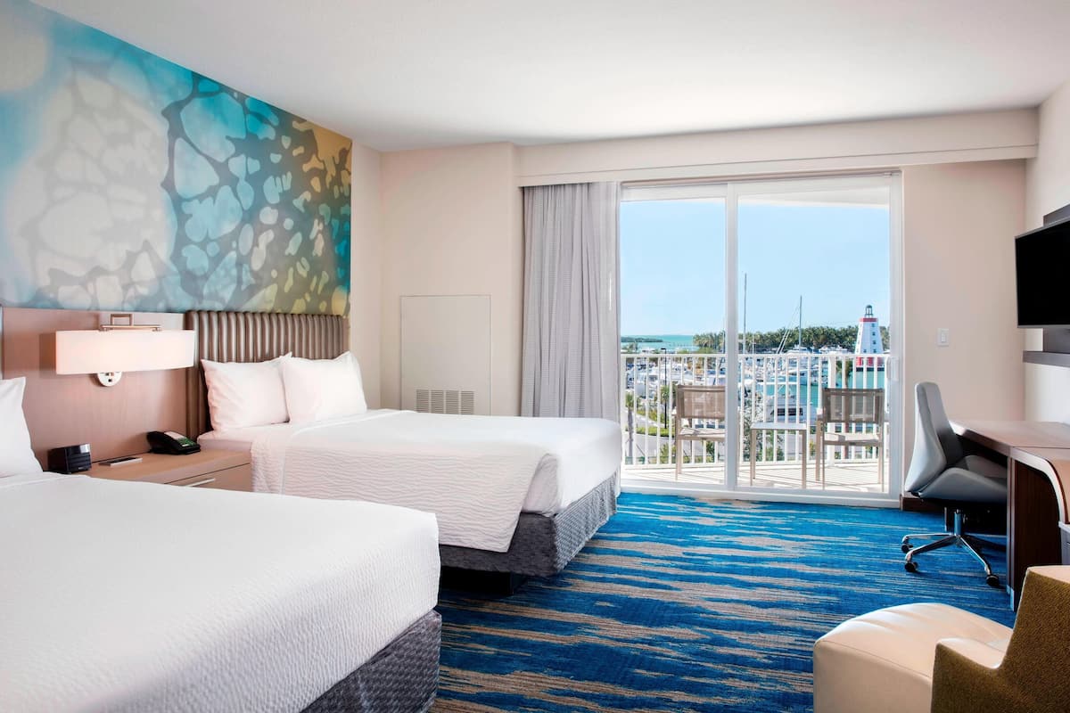 A hotel room with two beds, a desk, a chair, a TV, and a large window with a view of the city.