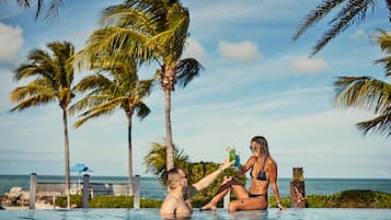 Um casal em uma piscina com vista para o oceano e palmeiras.