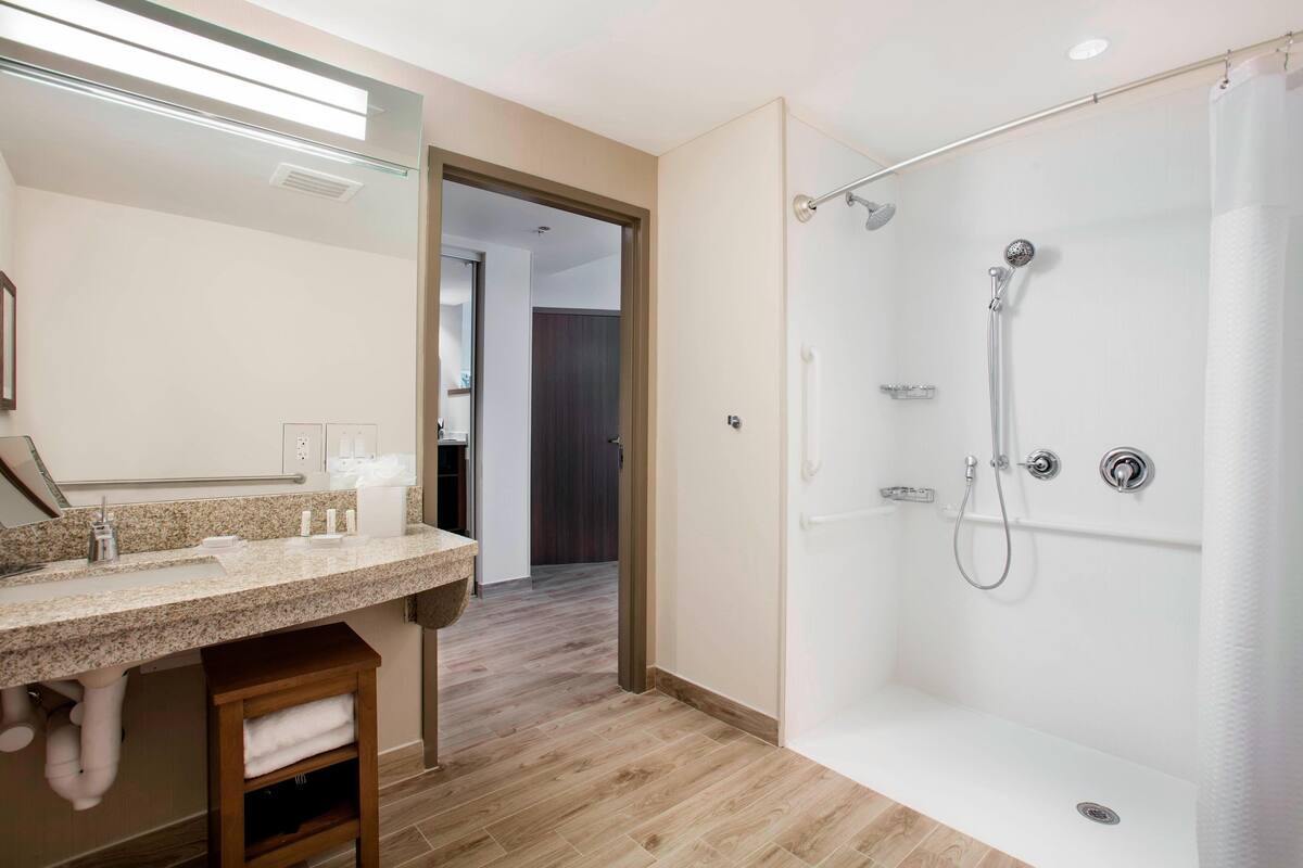 A modern bathroom with a glass-enclosed shower, a granite countertop, and a wooden stool.