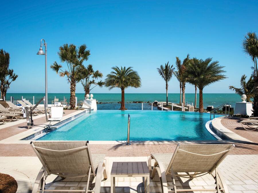 A poolside area with lounge chairs, palm trees, and a view of the sea.