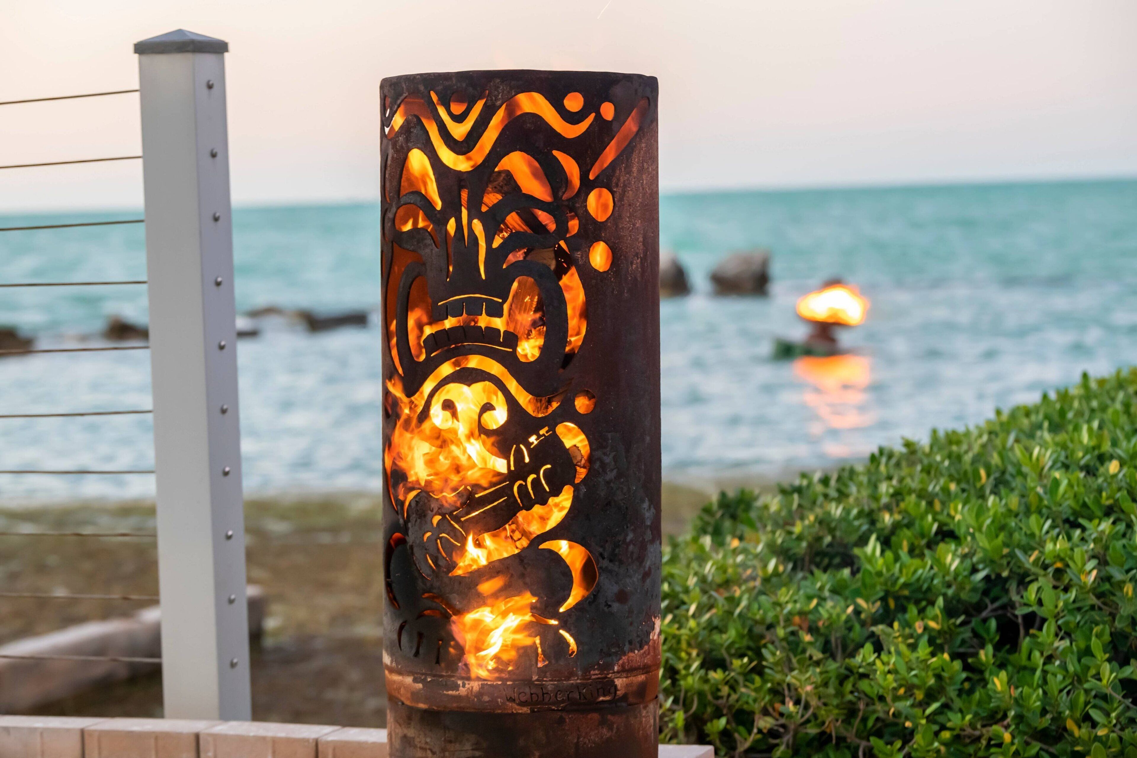 A decorative metal pillar with a carved design, located near a railing and a body of water.