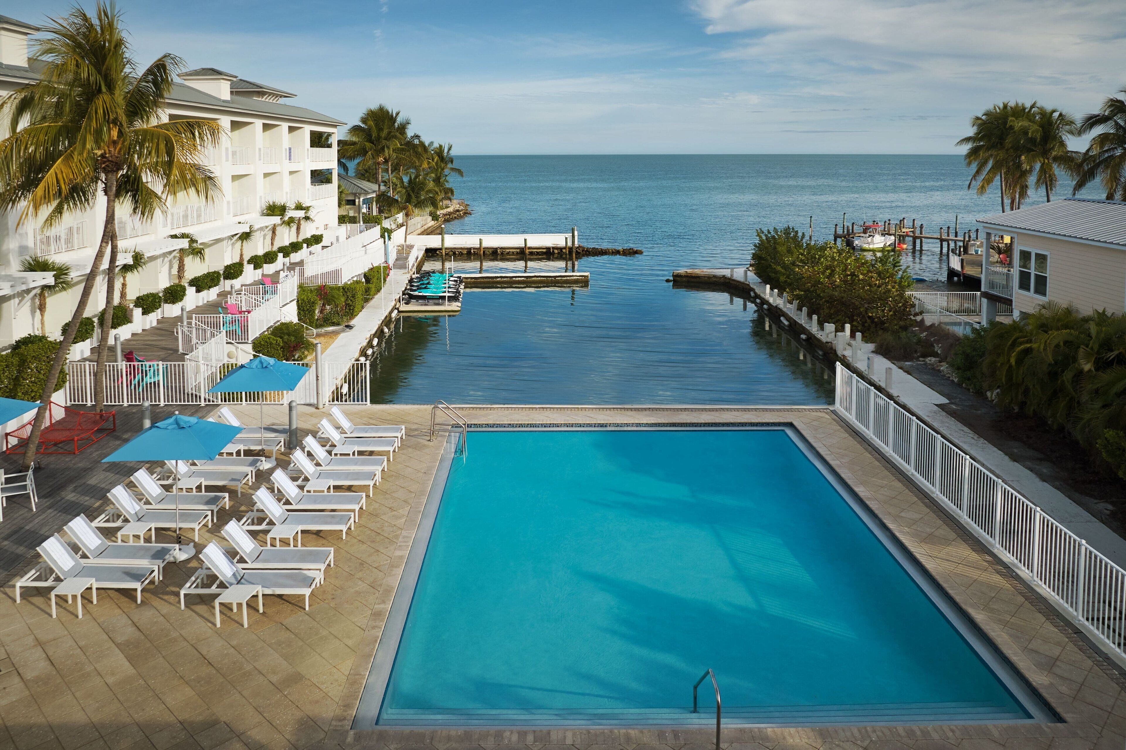 A pool area with lounge chairs and umbrellas, a dock, and a view of the ocean.