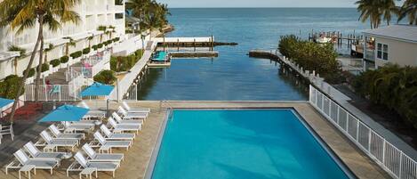 A pool area with lounge chairs and umbrellas, a dock, and a view of the ocean.