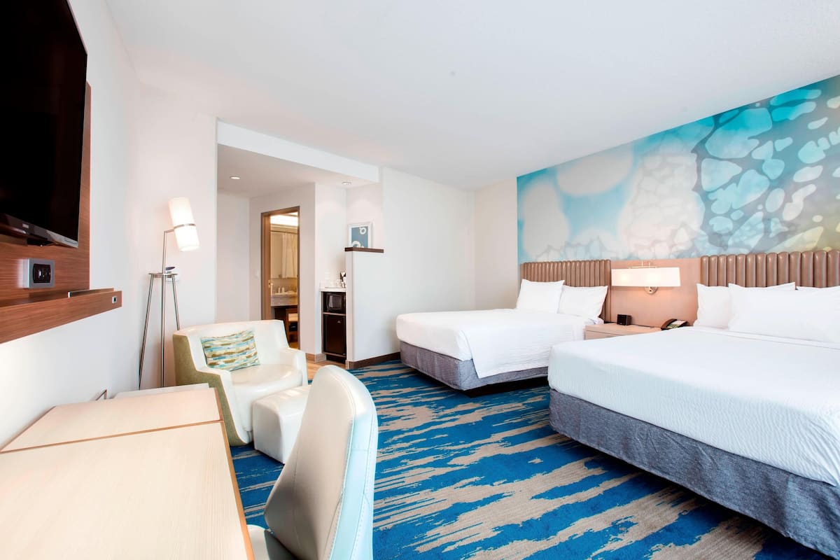 A hotel room with a large bed, a desk, a chair, and a wall with a blue and white abstract design.