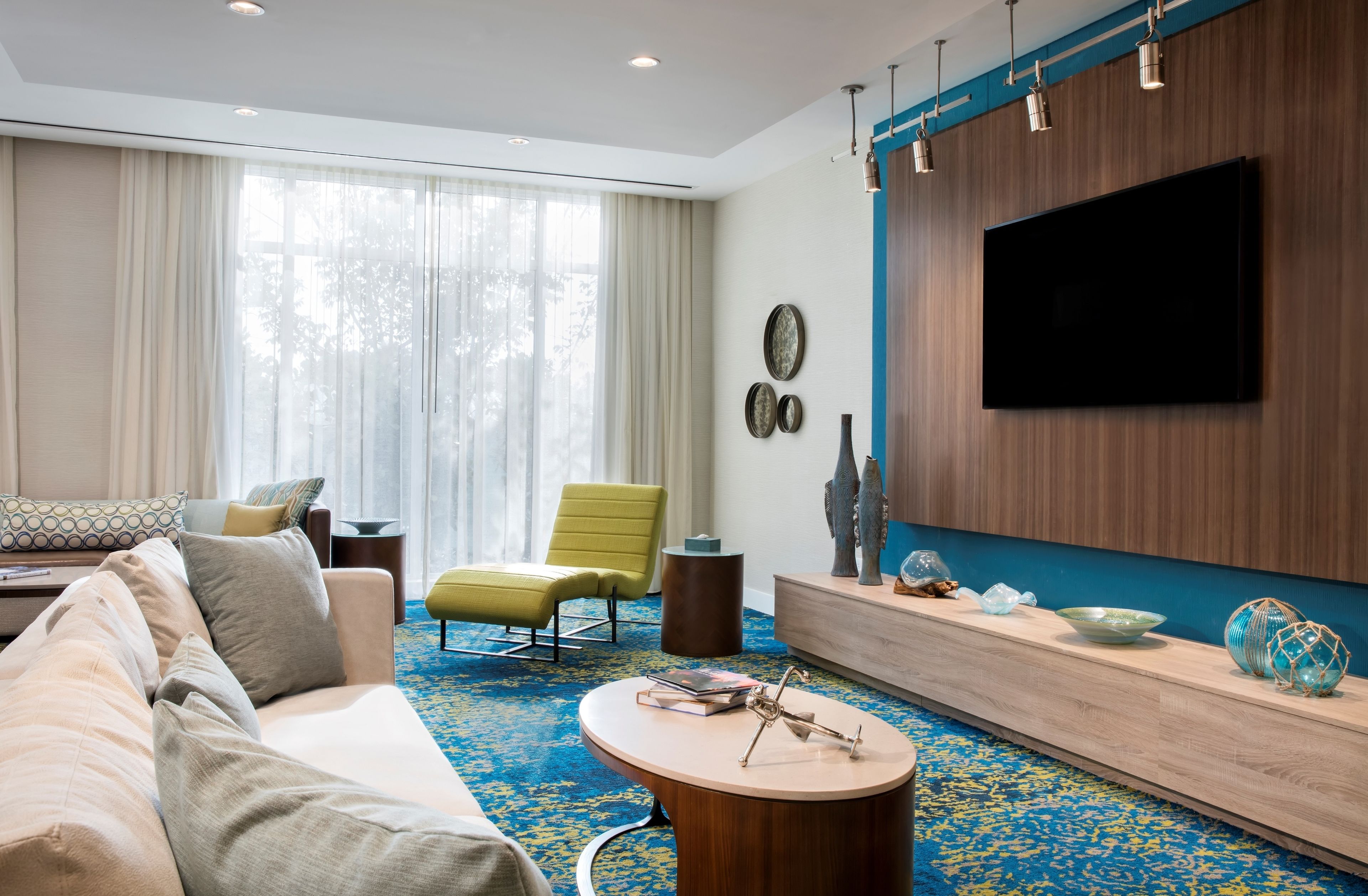 A modern living room with a sofa, armchair, coffee table, and a flat-screen TV mounted on a wooden wall.