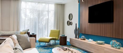 A modern living room with a sofa, armchair, coffee table, and a flat-screen TV mounted on a wooden wall.