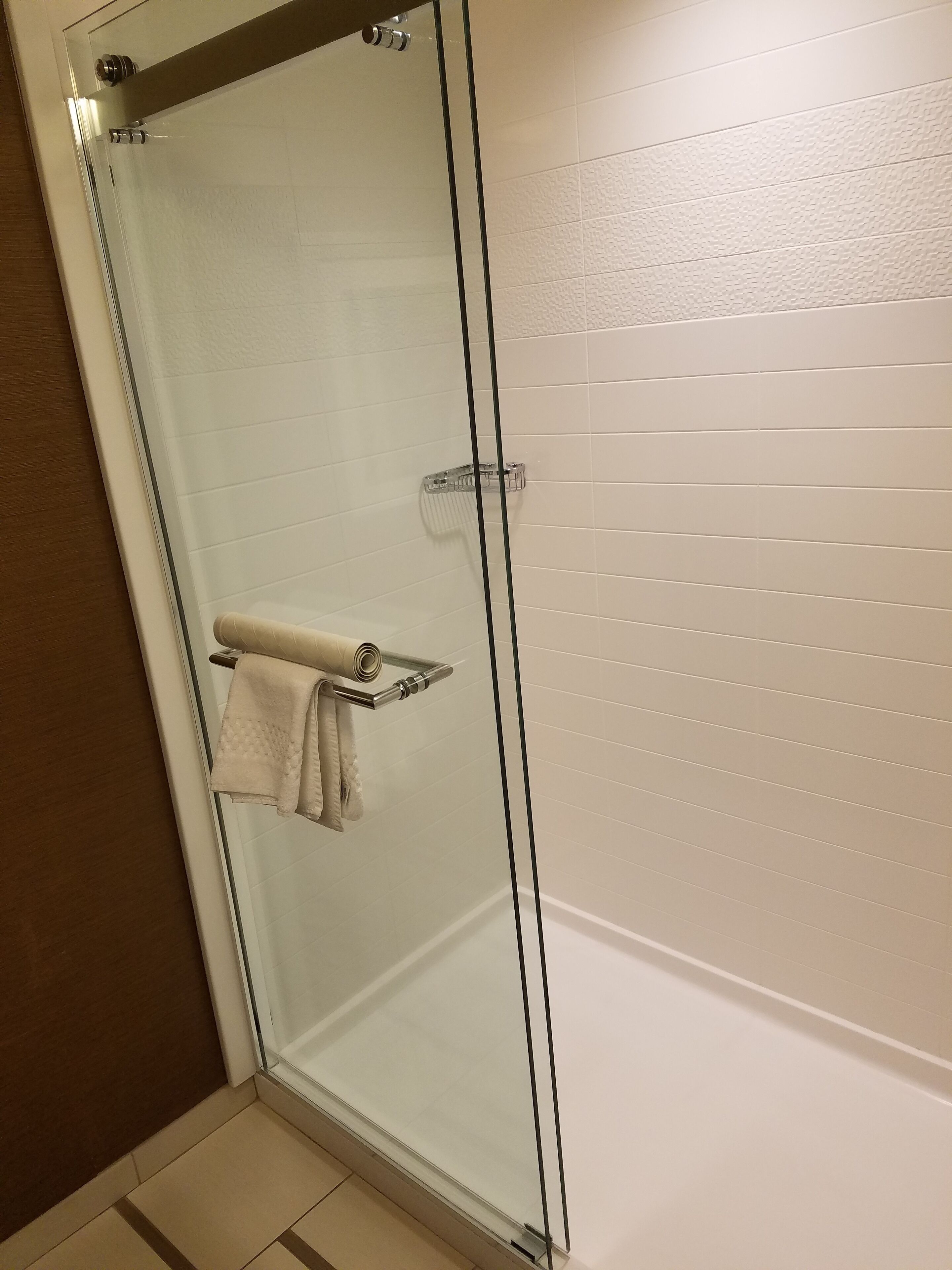Une douche fermée par des parois de verre, avec un porte-serviettes et un mur recouvert de carreaux blancs.