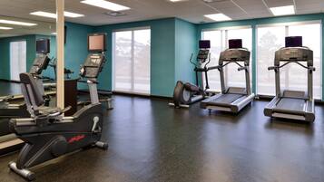 Un gimnasio con máquinas de cardio, un ventanal grande y una pared color turquesa.