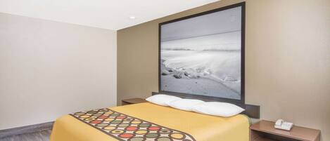 A hotel room with a bed, a nightstand, a painting of a beach scene, and a telephone on the nightstand.
