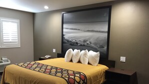Une chambre d’hôtel avec un grand lit, une table de chevet, une commode, un téléviseur fixé au mur et une fenêtre avec des stores.