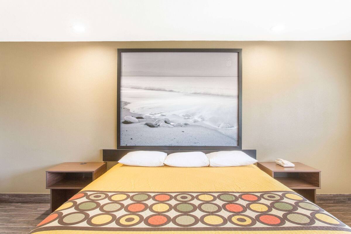 Une chambre d’hôtel avec un lit, un grand tableau encadré représentant une plage et une table de chevet avec un téléphone.
