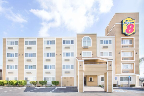 Un hotel de varios pisos con fachada color beige, un llamativo letrero de 'Super 8' y un estacionamiento al frente.