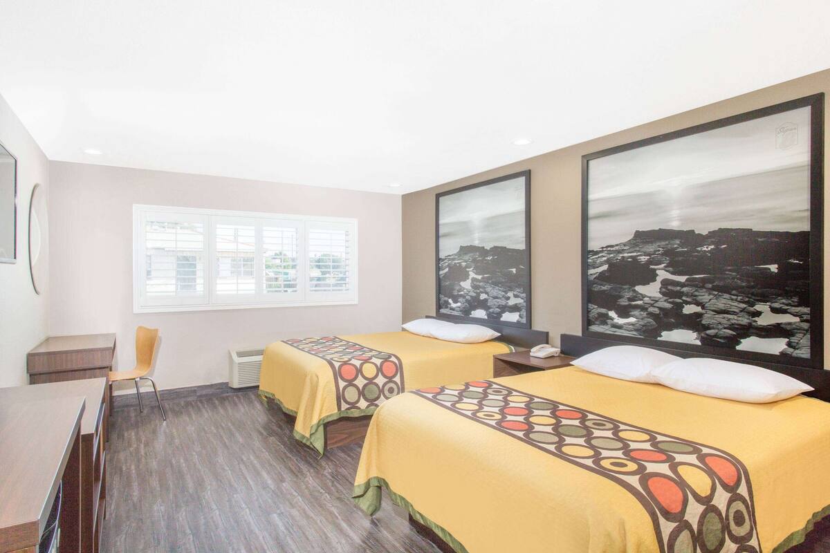 Une chambre d’hôtel avec deux lits, un bureau, une chaise et une grande fenêtre.