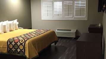 Habitación de hotel con cama, escritorio, silla, cesto de basura y ventana con persianas.