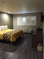 Habitación de hotel con cama, escritorio, silla, cesto de basura y ventana con persianas.