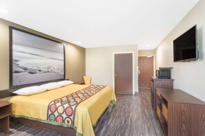 Una habitación de hotel con cama, televisión, puerta y un escritorio pequeño.