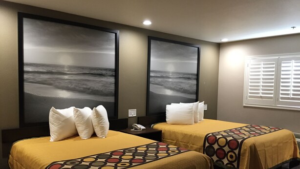 Une chambre d’hôtel avec deux lits, chacun recouvert d’une couvre-lit jaune et agrémenté d’oreillers blancs. Deux grandes œuvres d’art mural représentent une scène de plage.