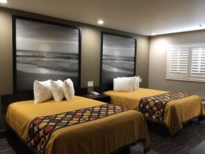Una habitación de hotel con dos camas, cada una con una colcha amarilla y almohadas blancas. Hay dos grandes cuadros murales que representan una escena de playa.