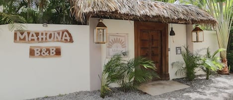 A small, rustic building with a thatched roof and a sign reading "MAHONA B&B".