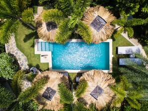 An aerial view of a resort with a rectangular swimming pool surrounded by thatched umbrellas and lush greenery. - Mahona Boutique Hotel (Las Terrenas)