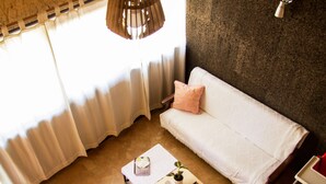 A cozy living room with a white sofa, a small table with a plant, and a pendant light. - Laranjalimao Guest House (Ponte de Lima)