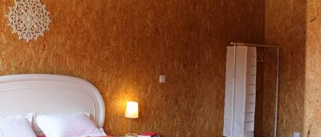 A bedroom with a wooden ceiling, a bed with white bedding, a bedside lamp, and a decorative wall piece.