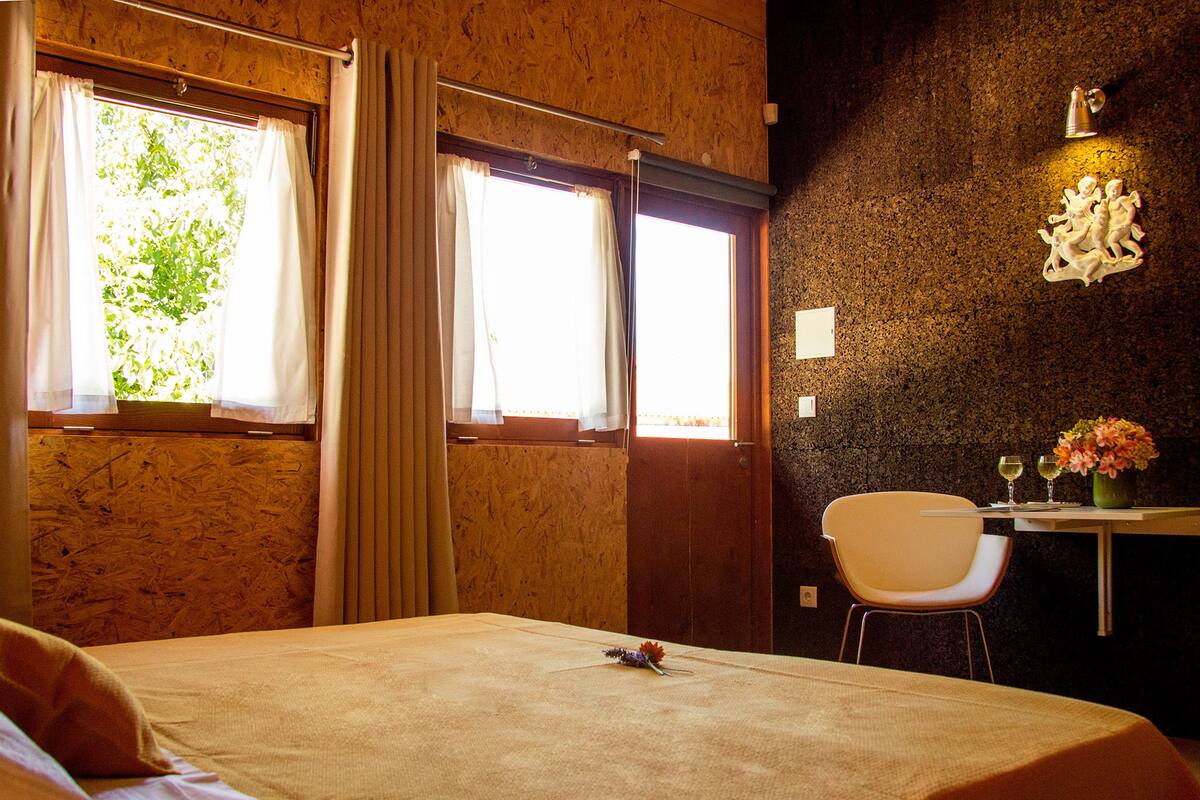Een kamer met een bed, een stoel, een tafel met twee glaasjes en een wandlamp.