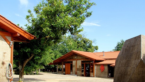 A courtyard with a cobblestone path leading to a building with a red-tiled roof and a large stone sculpture. - Laranjalimao Guest House (Ponte de Lima)
