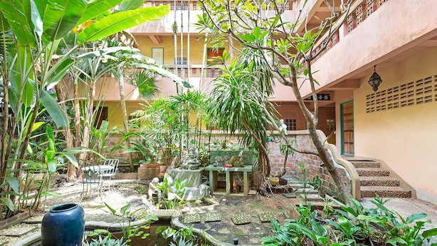 A courtyard with a small pond, potted plants, and a stone bench. - Casa Brazil Homestay & Gallery (Karon)