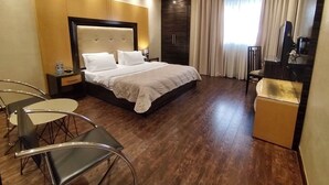 Habitación de hotel con una cama grande, un escritorio, una silla y una pequeña kitchenette.