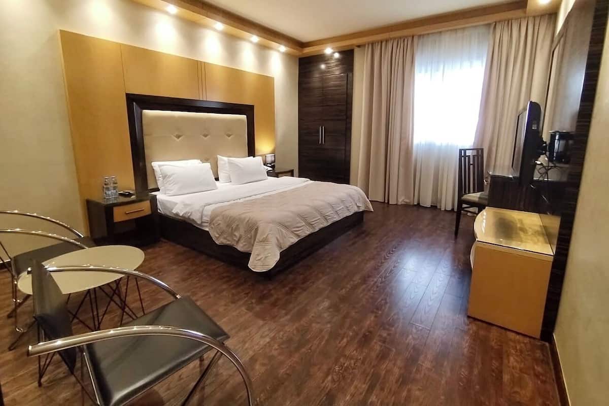 A hotel room with a large bed, a desk, a chair, and a small kitchenette.