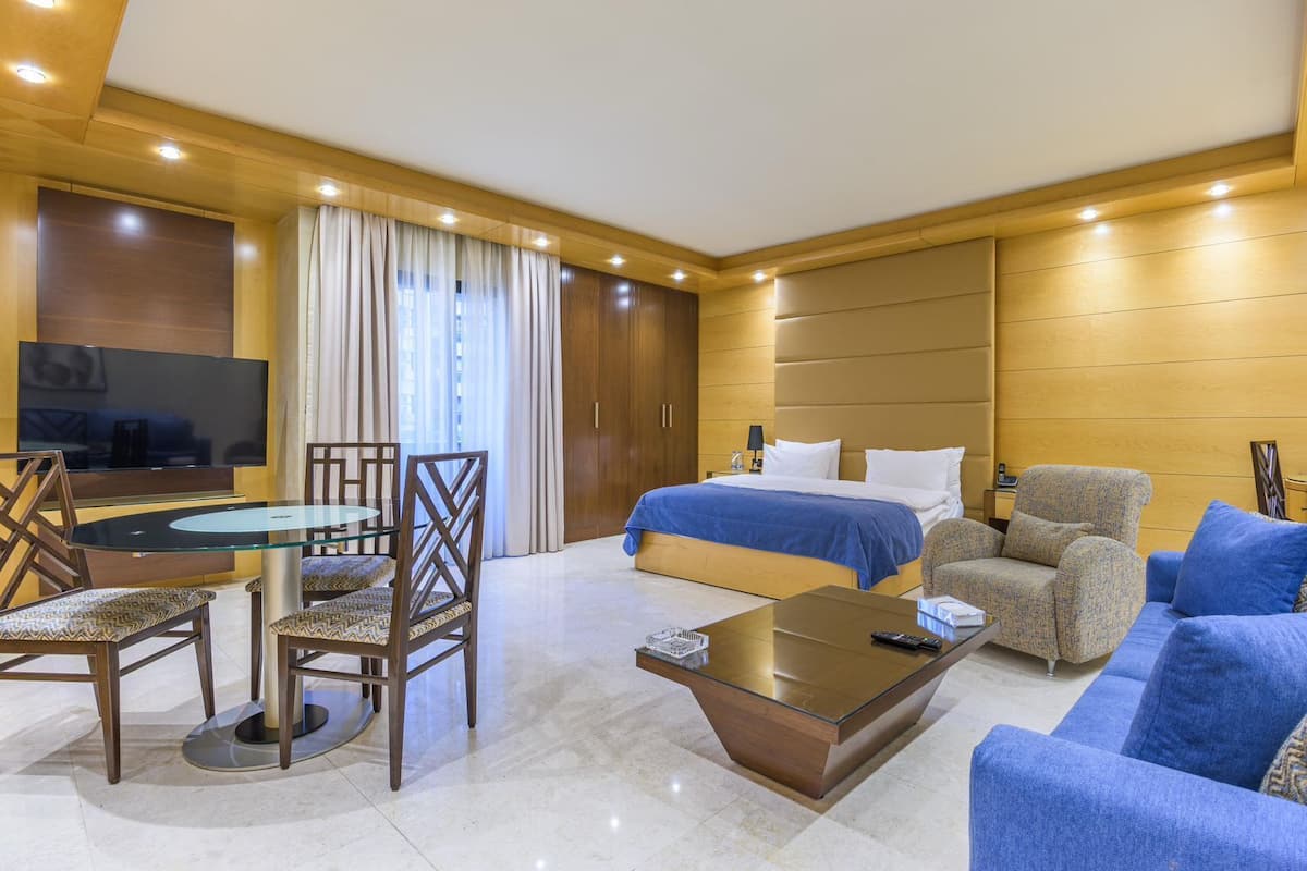 A modern hotel room with a bed, seating area, TV, and a dining table.