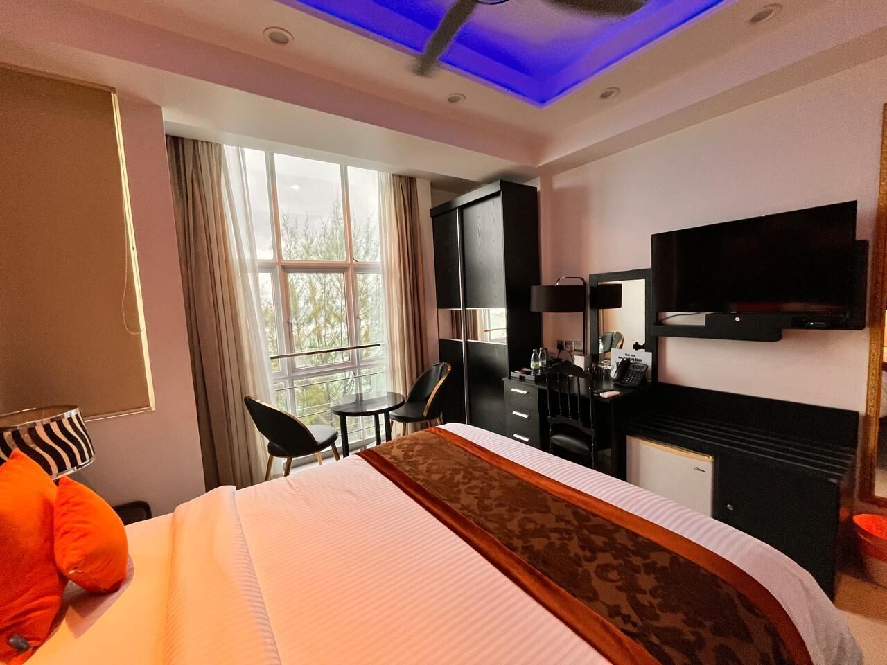 A hotel room with a bed, a desk, a chair, a TV, and a window with curtains.