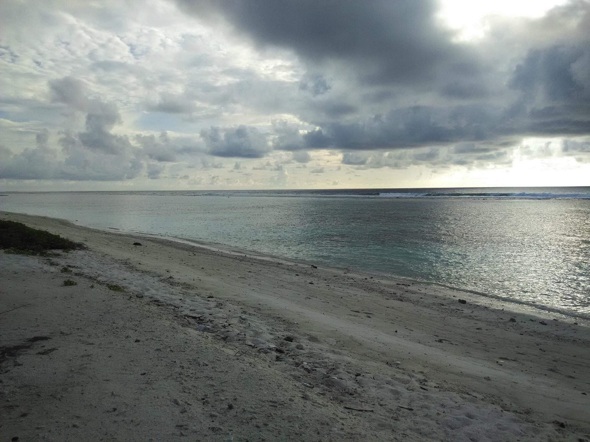 Una playa con orilla arenosa y agua tranquila bajo un cielo nublado.