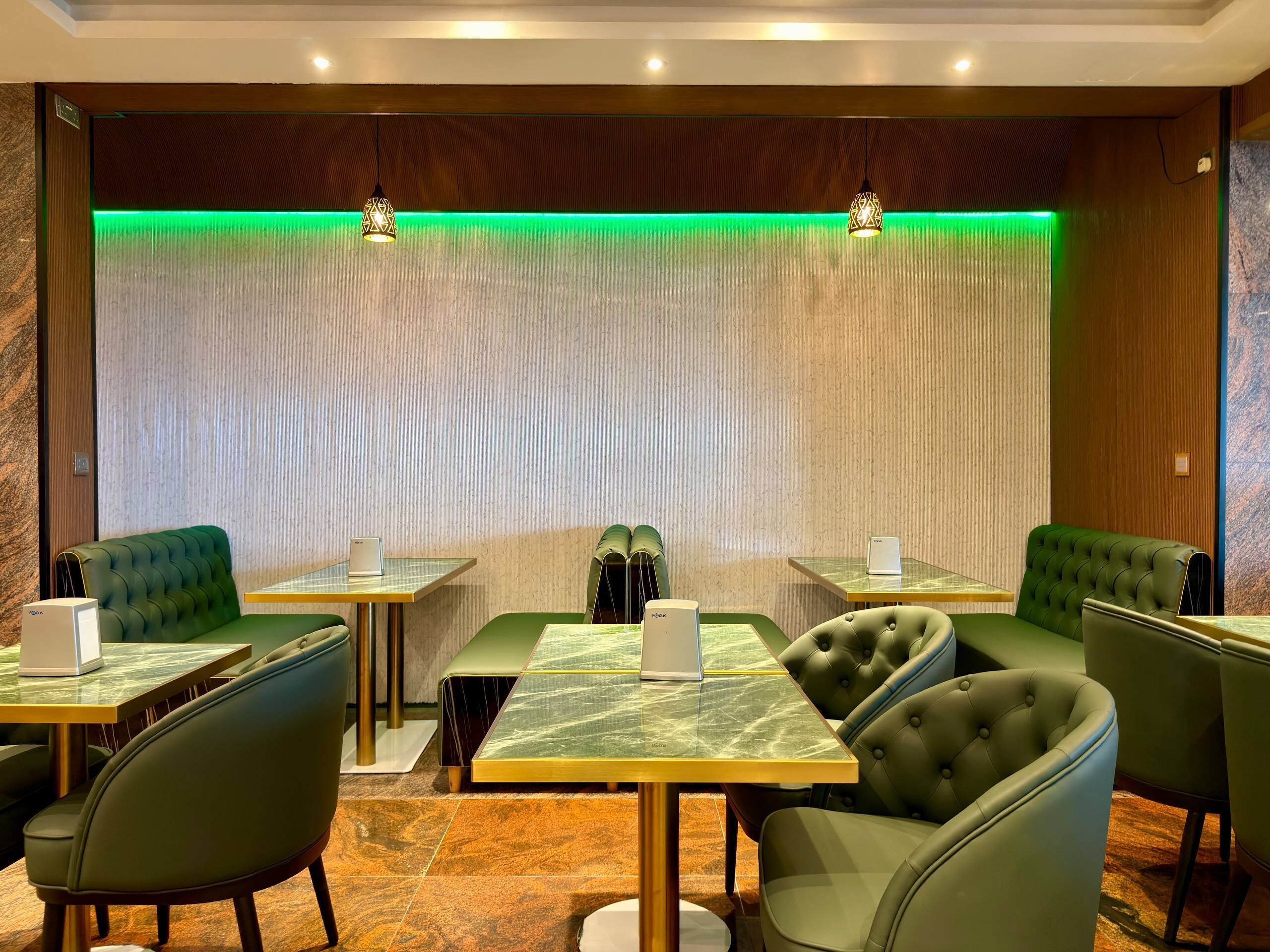 Un restaurante con asientos tapizados en verde, mesas con cubierta de mármol y una tira de luz ambiental verde.
