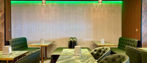 Un restaurante con asientos tapizados en verde, mesas con cubierta de mármol y una tira de luz ambiental verde.