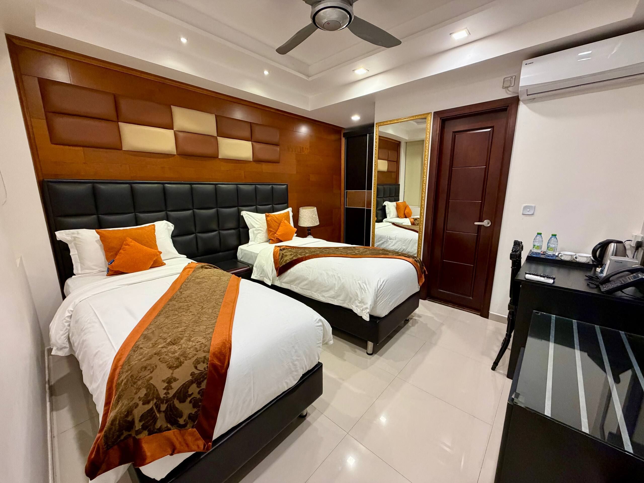 A hotel room with two beds, a desk, a mirror, and an air conditioning unit.