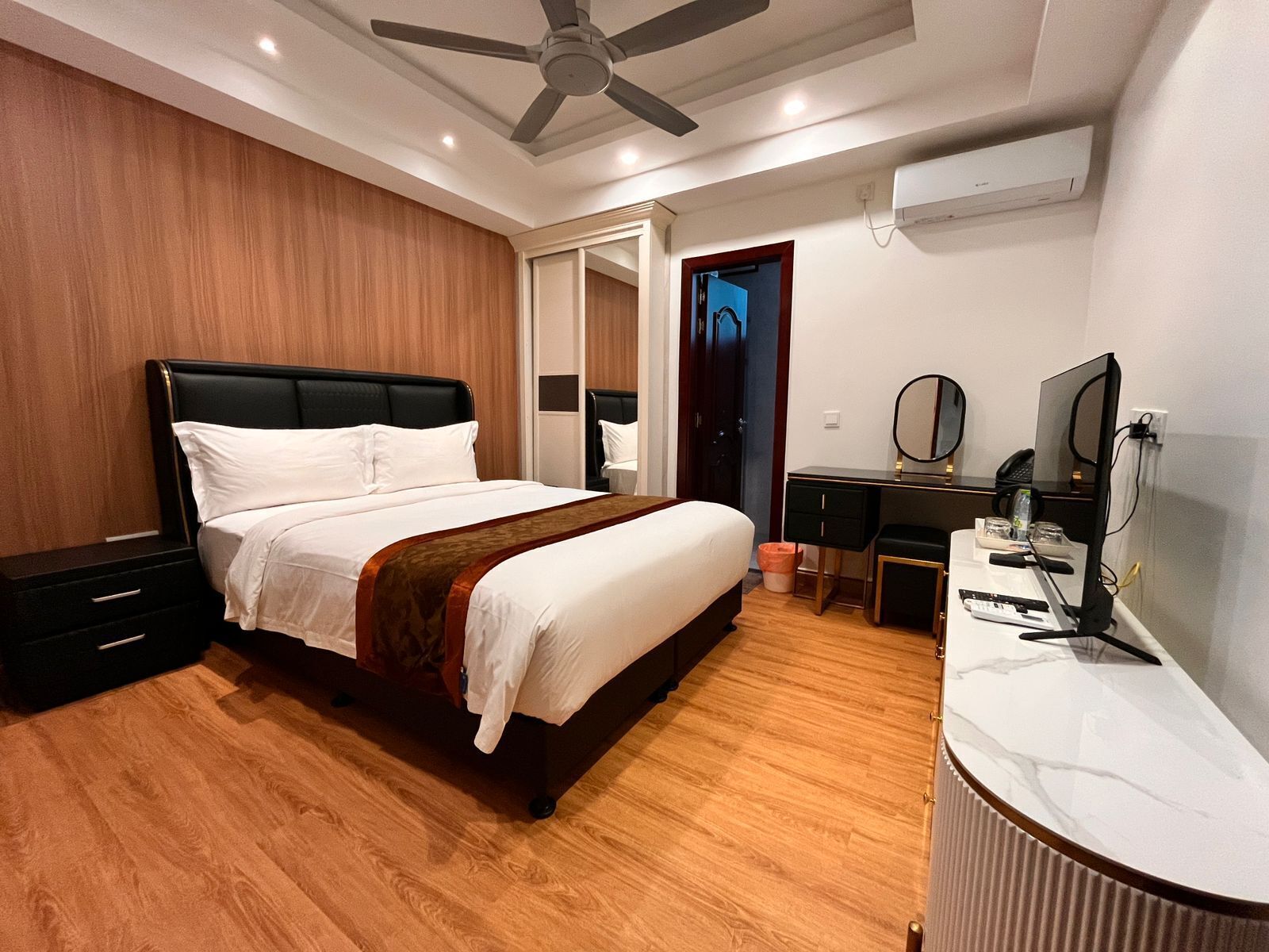 A modern hotel room with a large bed, a desk, a chair, a wardrobe, and a ceiling fan.