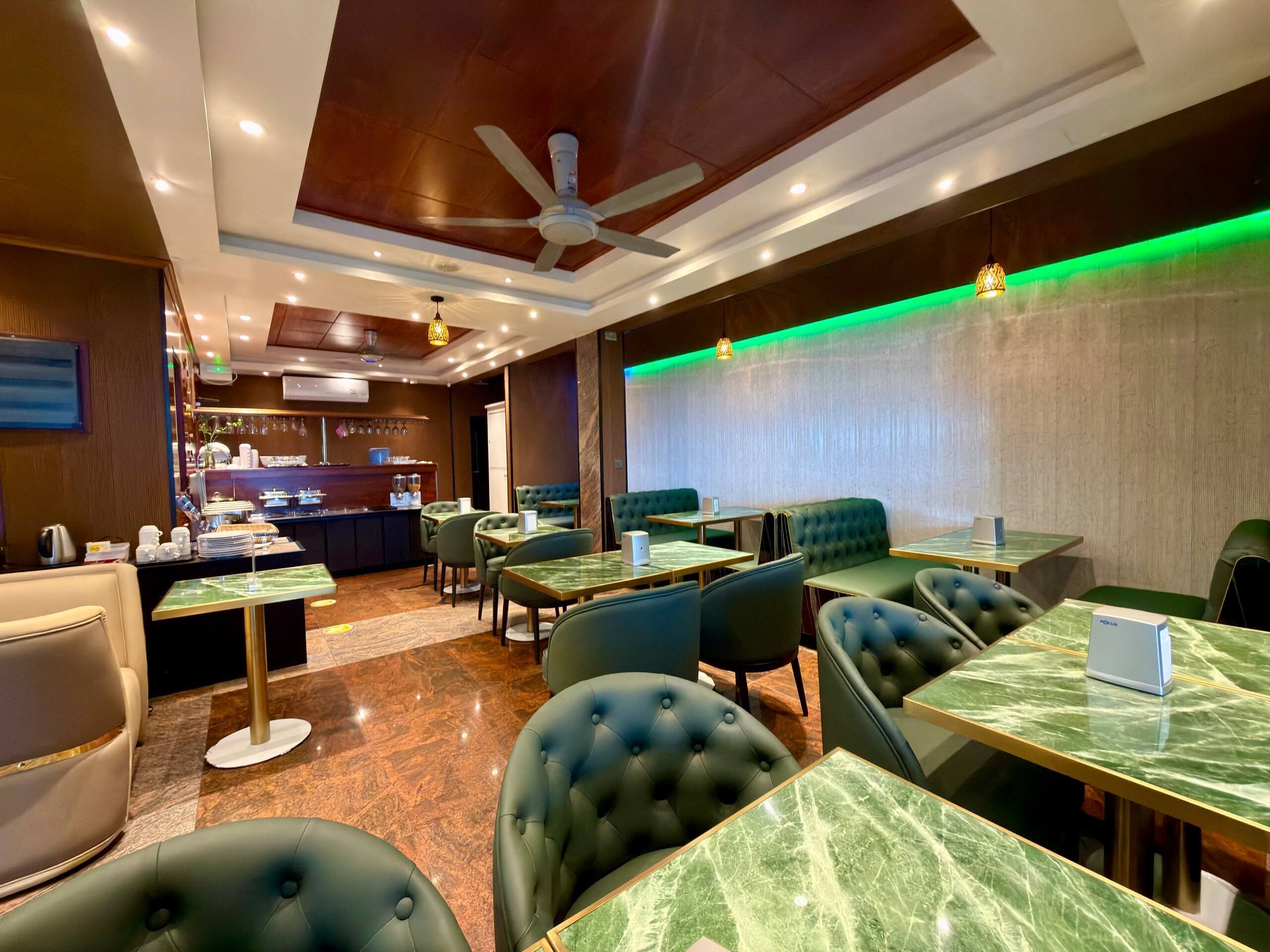 A restaurant with marble-topped tables and green upholstered booths.